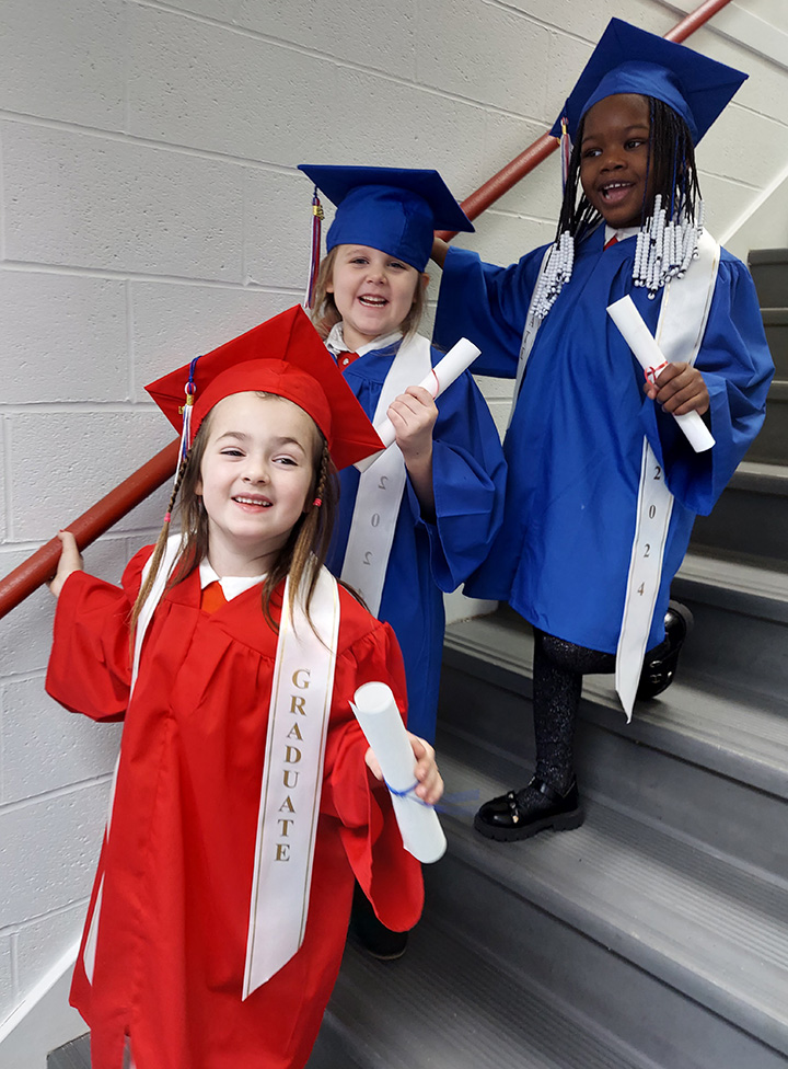 Kindergarteners graduating in their red and blue caps and gowns